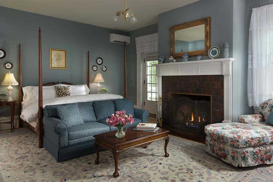 Cozy bedroom with a blue color scheme, a four-poster bed, a floral armchair, and a fireplace.