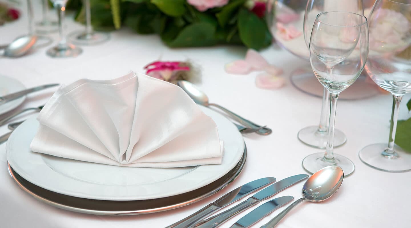 A neatly arranged dining table with a white folded napkin on a plate, accompanied by silverware and elegant glassware.