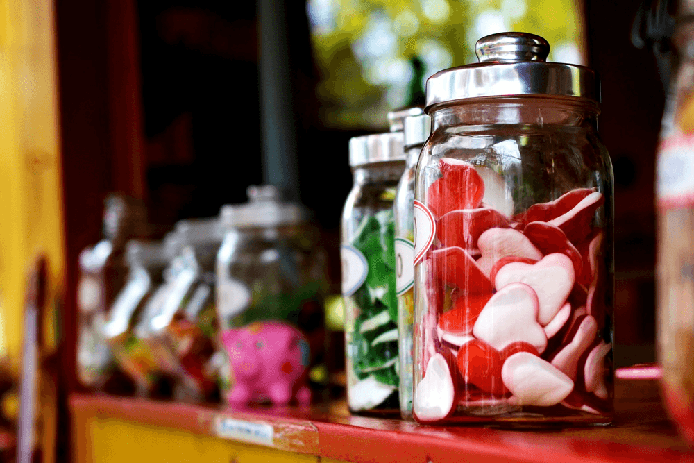 Glass jars filled with colorful heart-shaped candies on a wooden shelf.