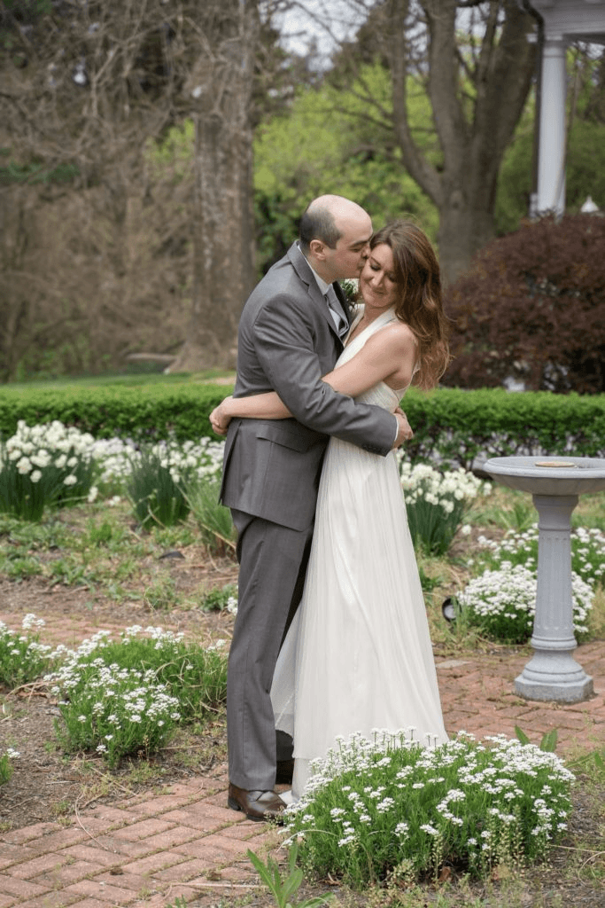 A couple embraces joyfully in a garden filled with blooming flowers.