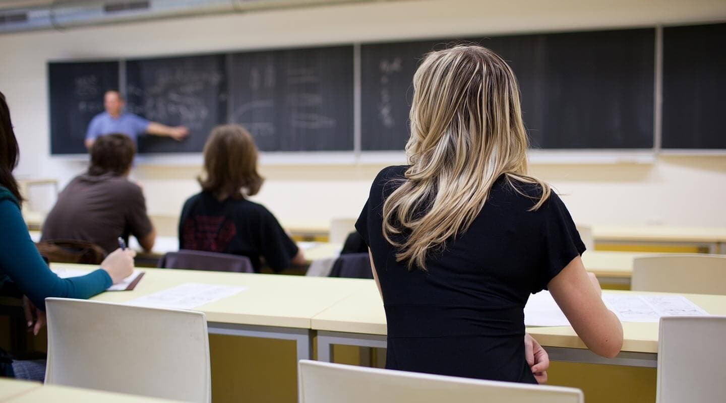 Students listening to a teacher in a classroom setting.