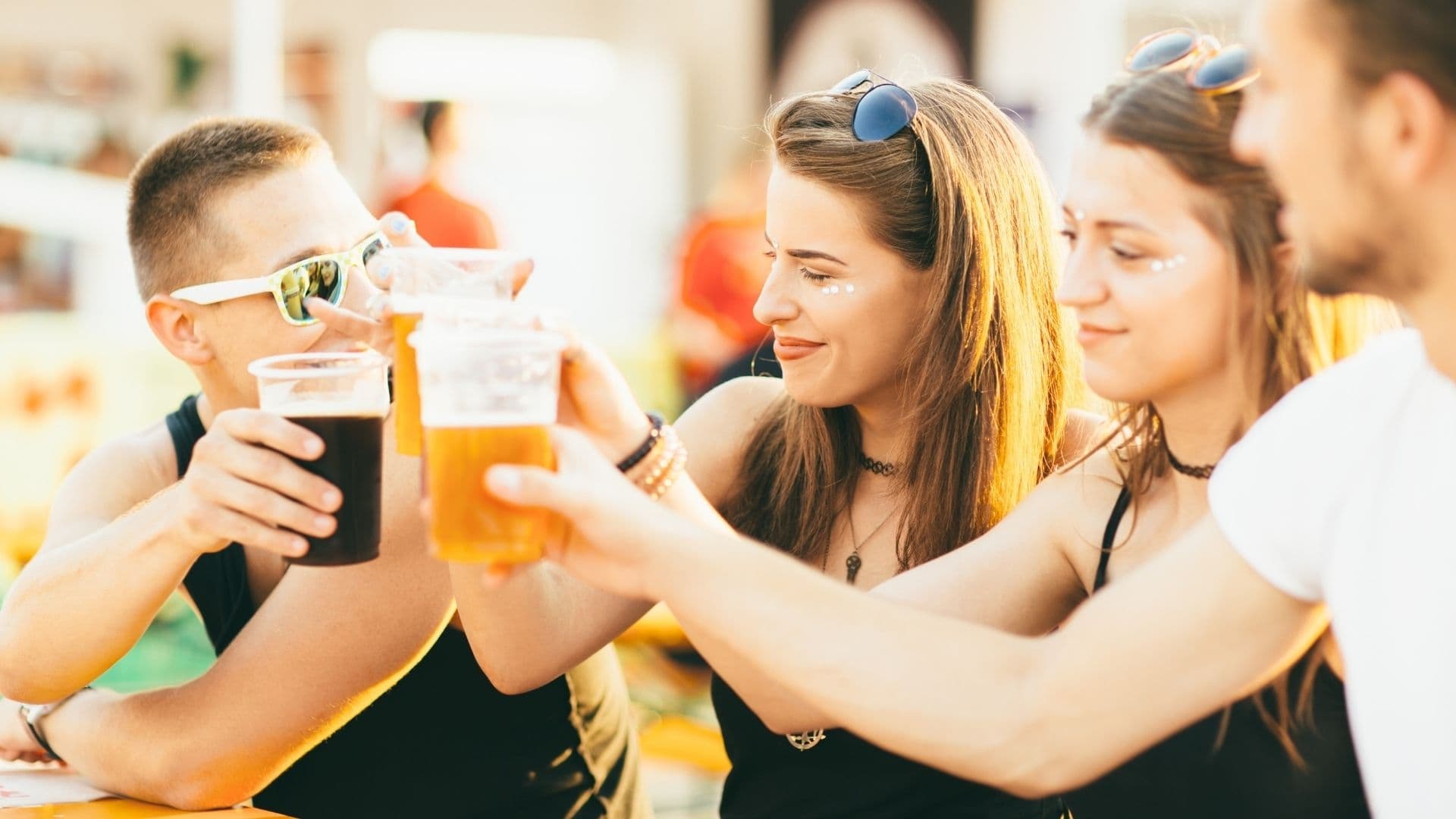 A group of friends toast with cups of beer in a lively outdoor setting.