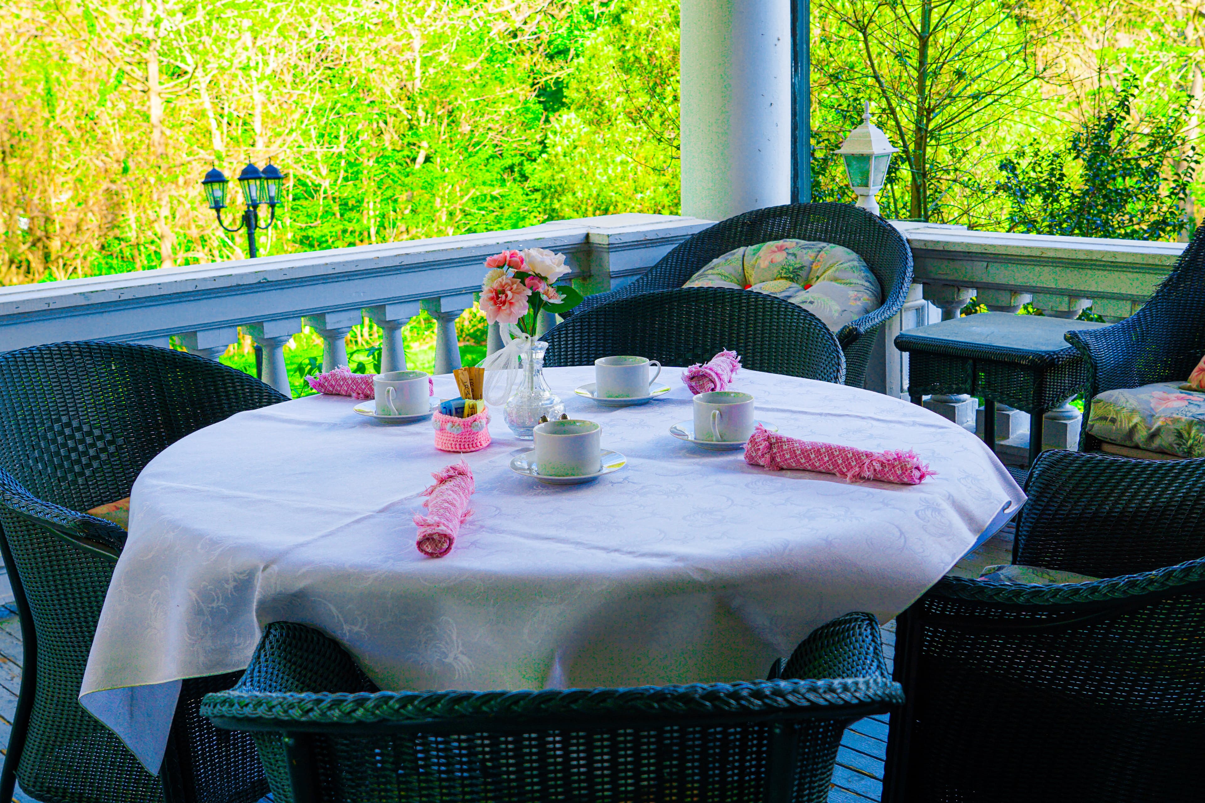 A beautifully set outdoor table with tea cups and floral decor, surrounded by wicker chairs.