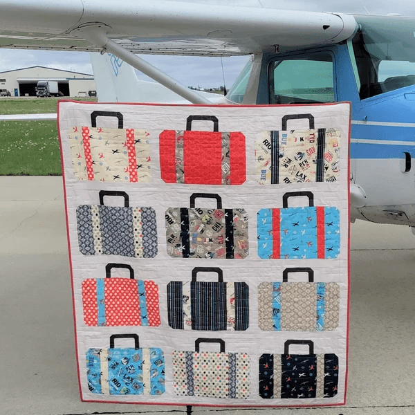 A colorful quilt featuring a pattern of various suitcases displayed in front of an airplane.