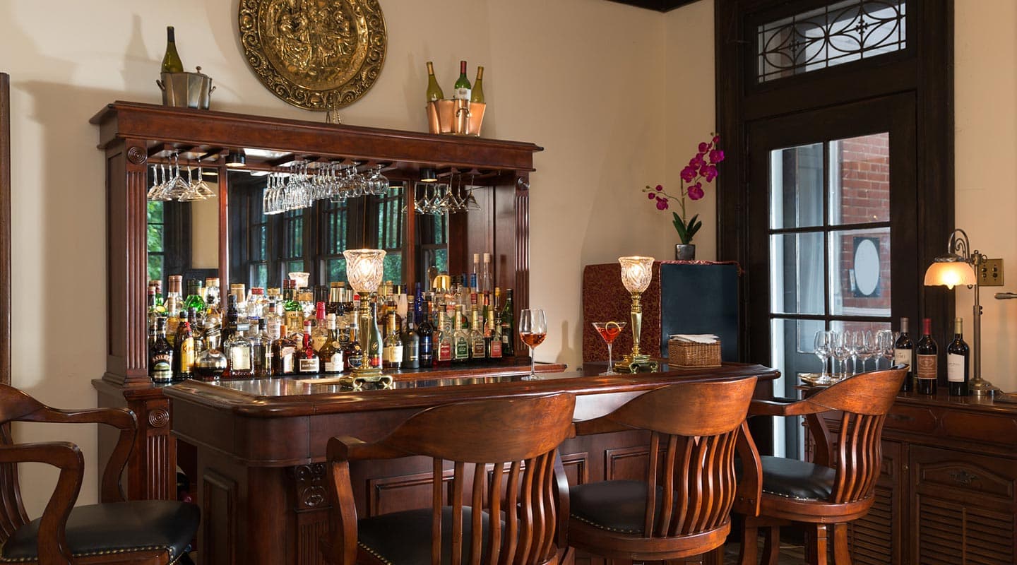 A polished wooden bar with an array of liquor bottles and glasses, complemented by elegant seating.