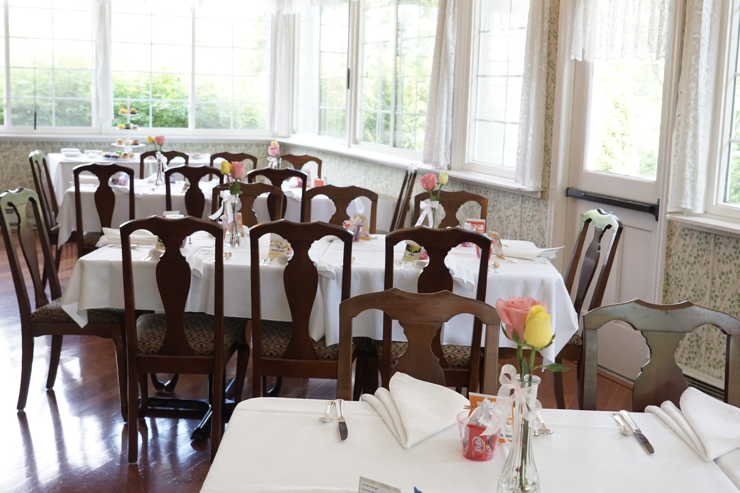 A bright dining room with neatly set tables and floral centerpieces.