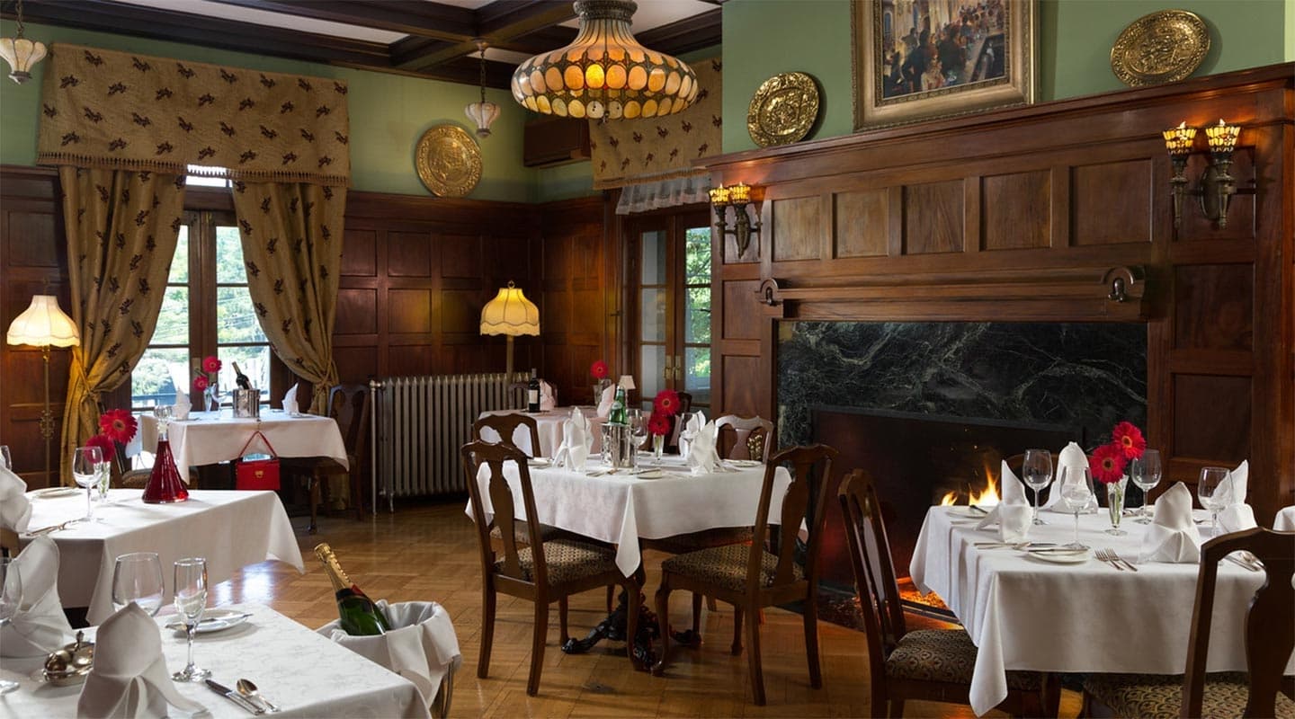 Elegant dining room with wooden paneling, white tablecloths, and a warm fireplace.