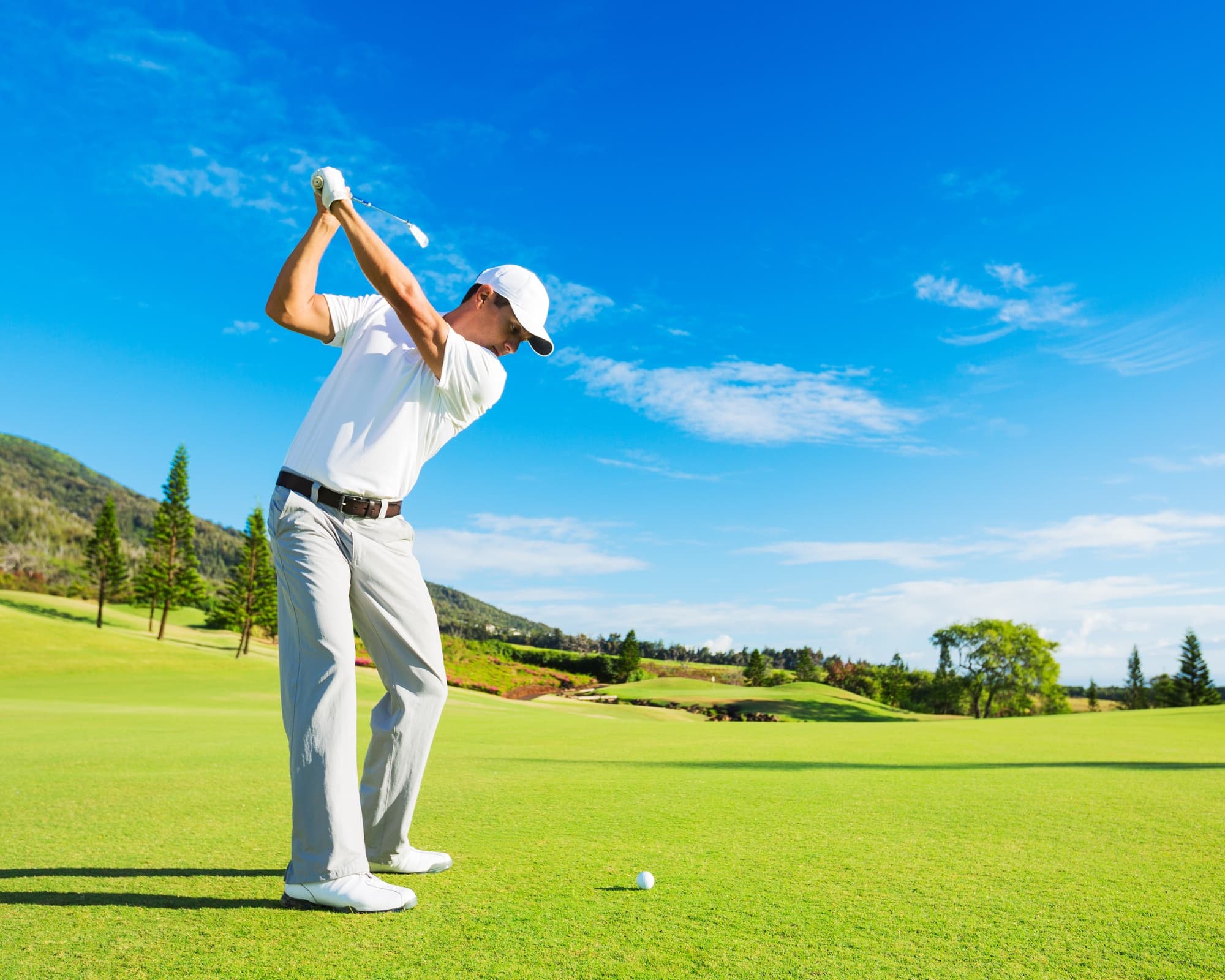 A golfer swings a club on a sunny day at a lush green course.