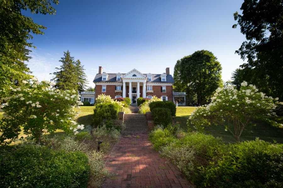 A grand brick mansion surrounded by lush greenery and blooming flowers.
