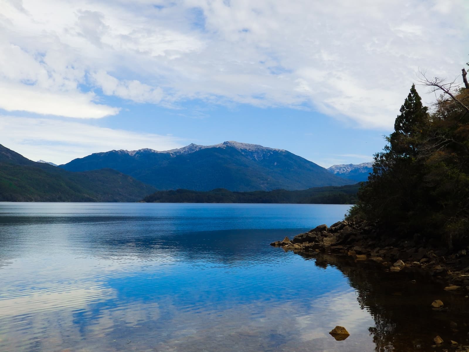Serene lake reflecting mountains under a partly cloudy sky.