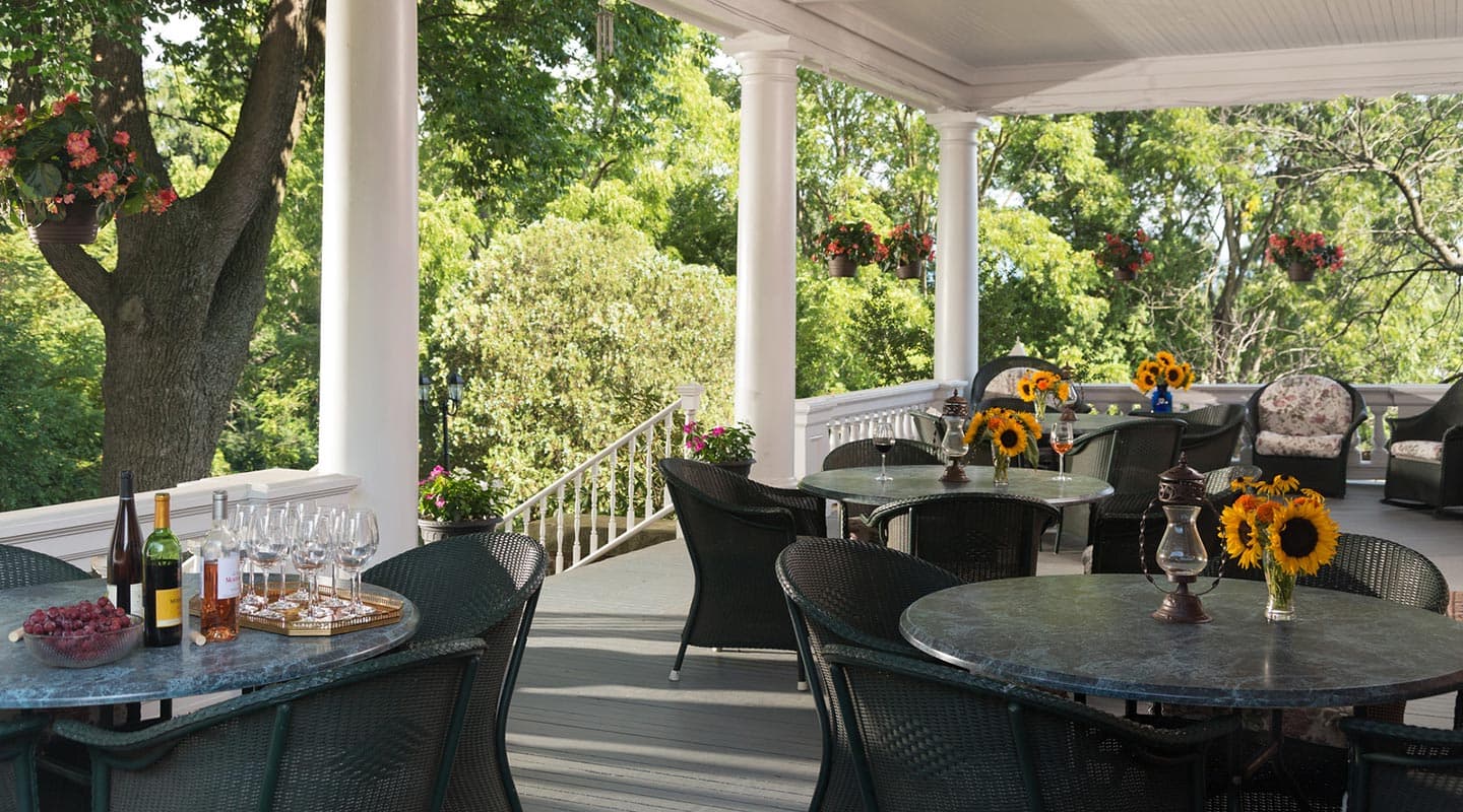 A cozy outdoor patio featuring tables with sunflowers, wine glasses, and a view of lush greenery.