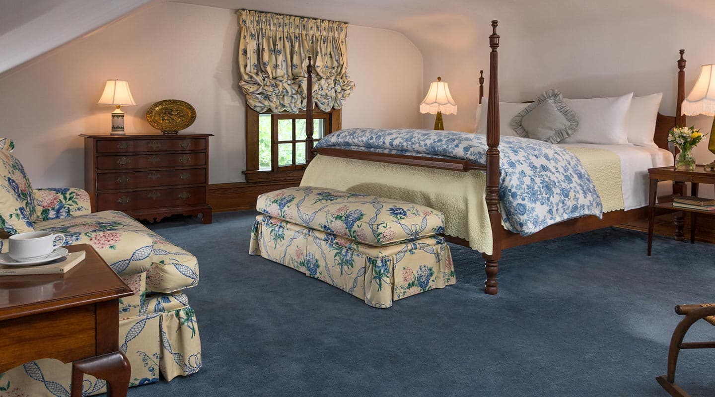 Cozy attic bedroom featuring a four-poster bed, floral-patterned furnishings, and soft lighting.