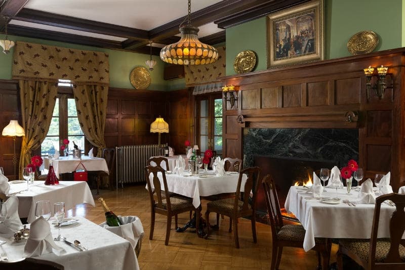 A cozy dining room with neatly set tables, elegant decor, and a fireplace.