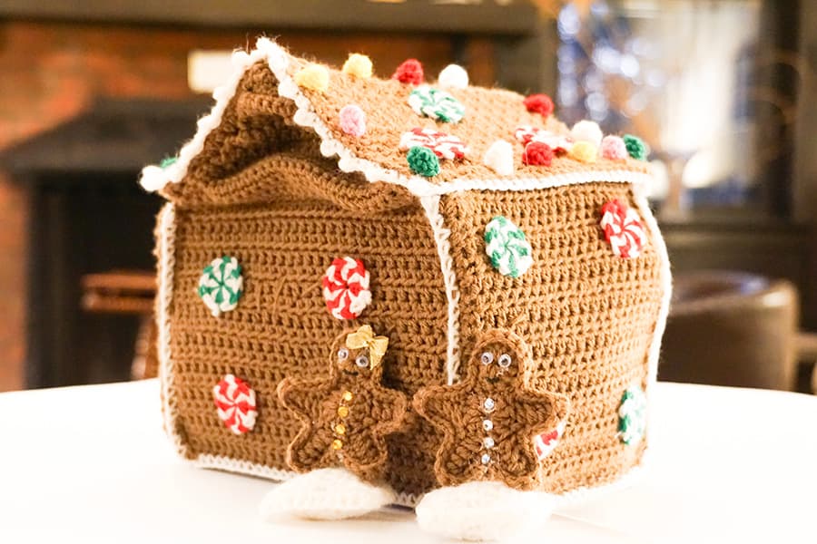 A crocheted gingerbread house adorned with colorful decorations and two gingerbread figures.