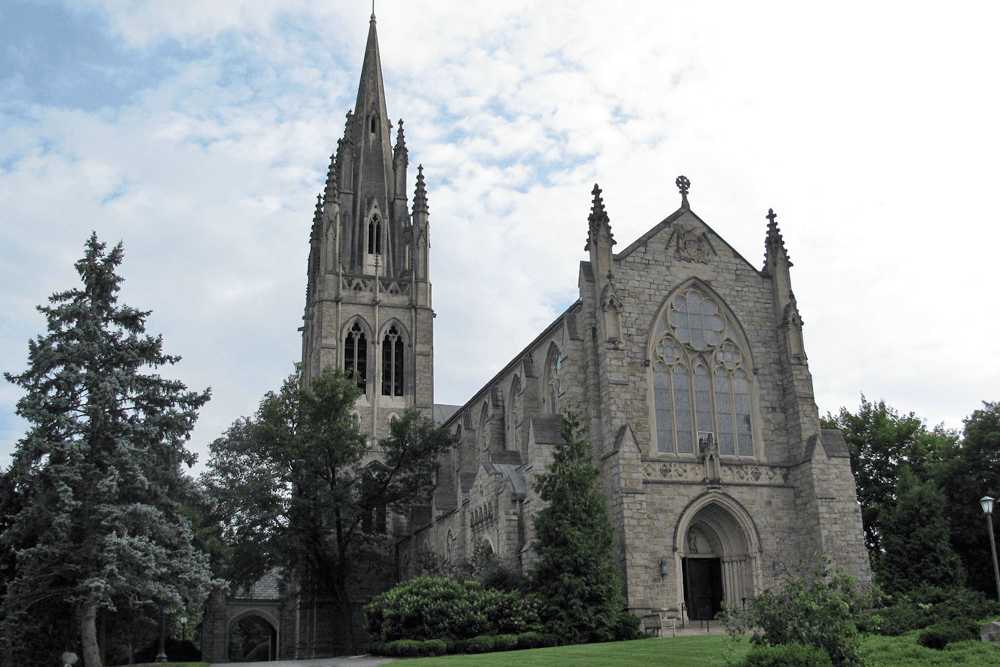 Gothic-style stone church surrounded by trees under a cloudy sky.