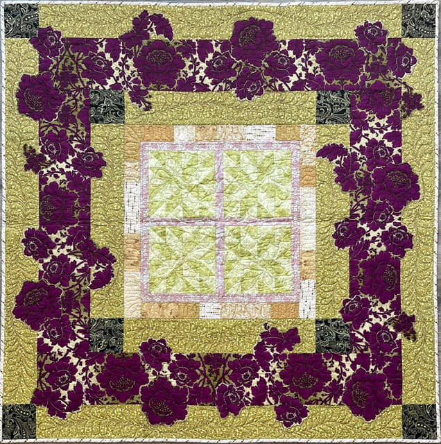 A colorful quilt featuring floral patterns in shades of purple and gold, with a central green patchwork design.