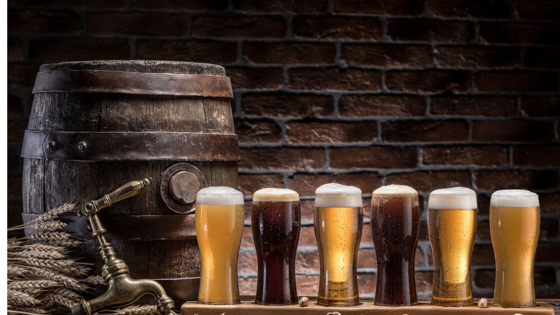 A wooden barrel next to six glasses of different styles of beer on a rustic backdrop.