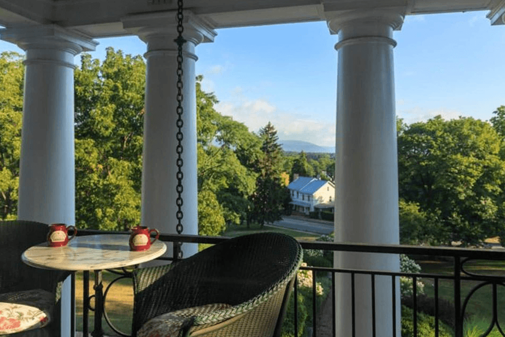 A balcony overlooking lush greenery and distant mountains, with a small table and two chairs.