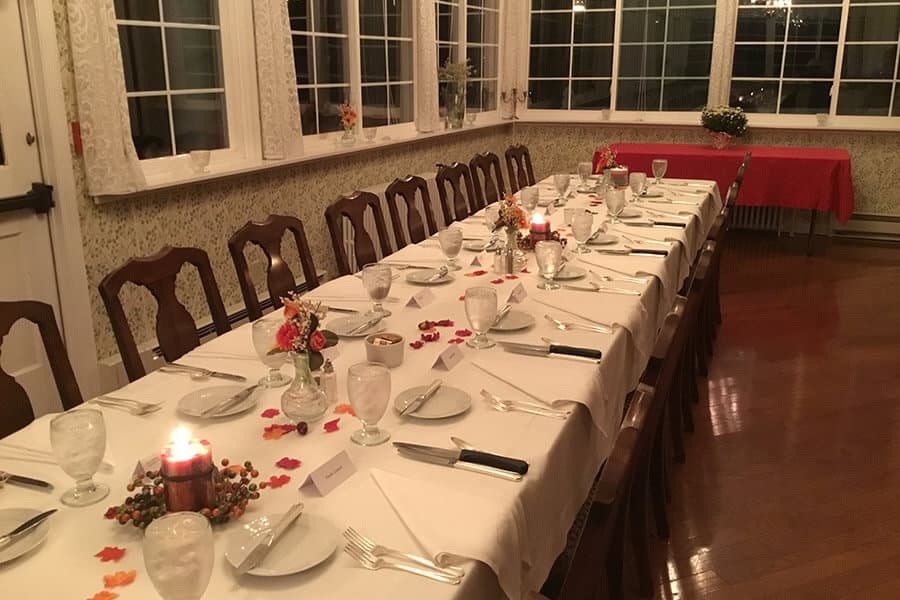 A long dining table is set with dishes, glasses, and decorative candles in a warmly lit room.