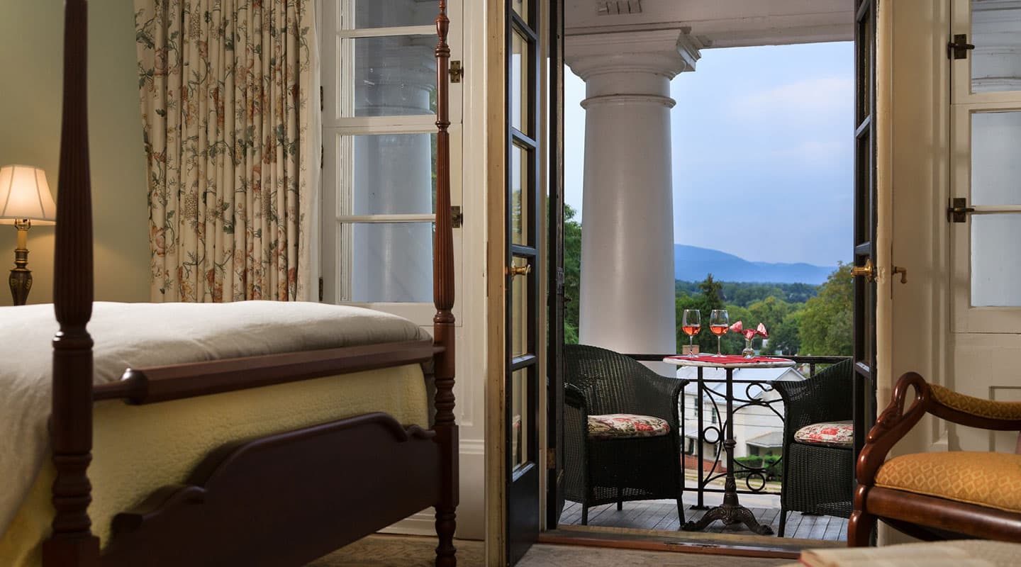 A cozy bedroom opens to a balcony overlooking green hills and a cloudy sky.