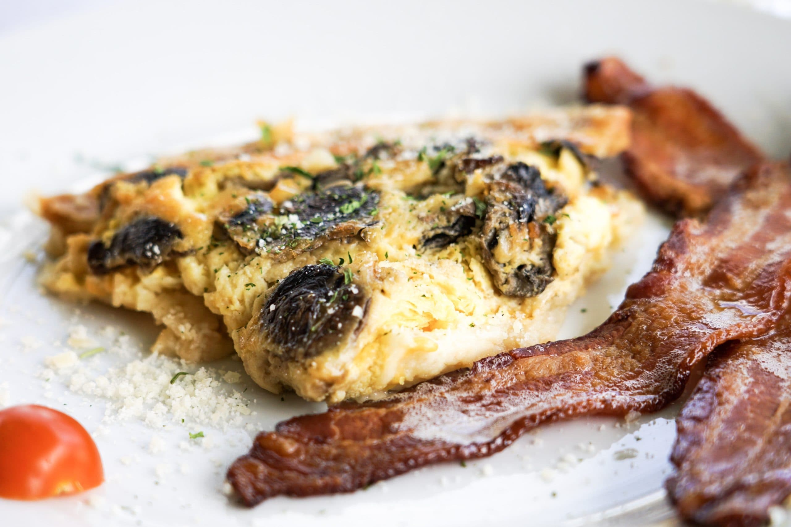 Close-up of a plate featuring an omelet with mushrooms and crispy bacon on the side.