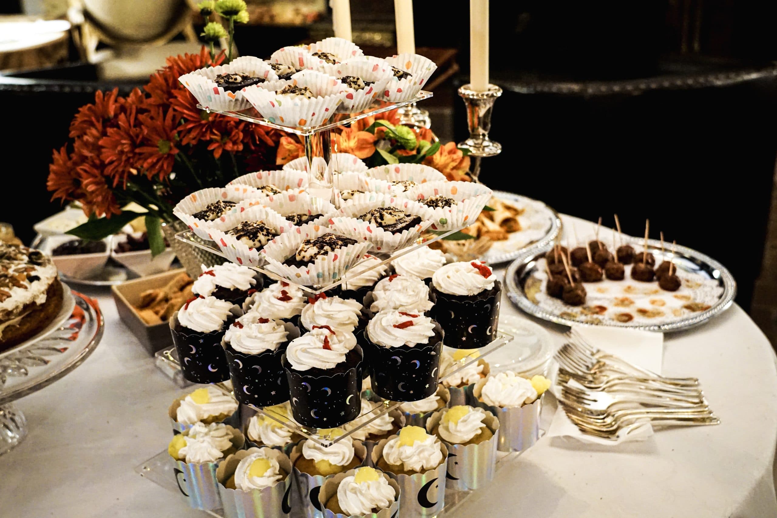 A tiered display of various decorated cupcakes and desserts on a table adorned with flowers.