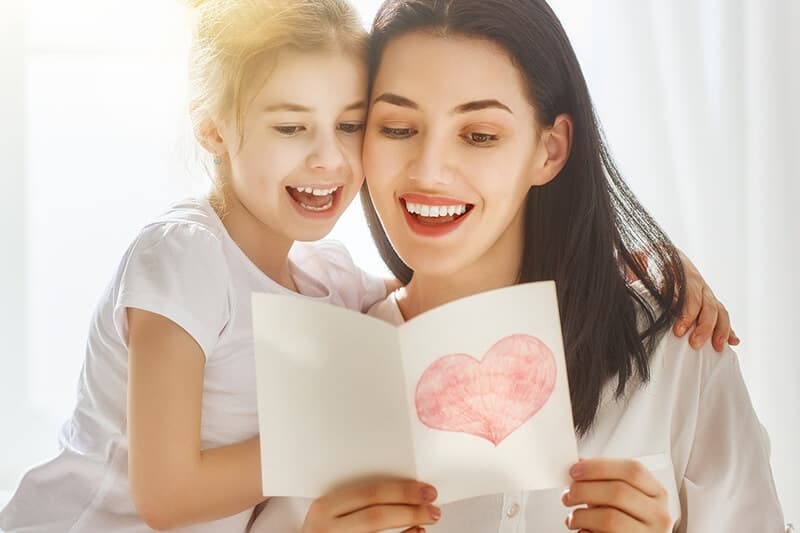 A mother and daughter joyfully share a moment as they read a card featuring a heart design.