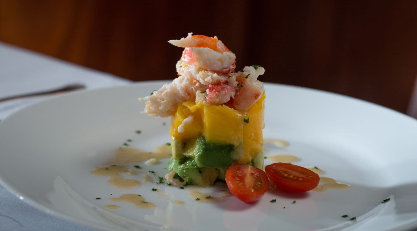 A gourmet dish of layered mango, avocado, and crab meat on a white plate. Garnished with cherry tomato halves and herbs, it conveys elegance and freshness. A gourmet dish of layered mango, avocado, and crab meat on a white plate. Garnished with cherry tomato halves and herbs, it conveys elegance and freshness.