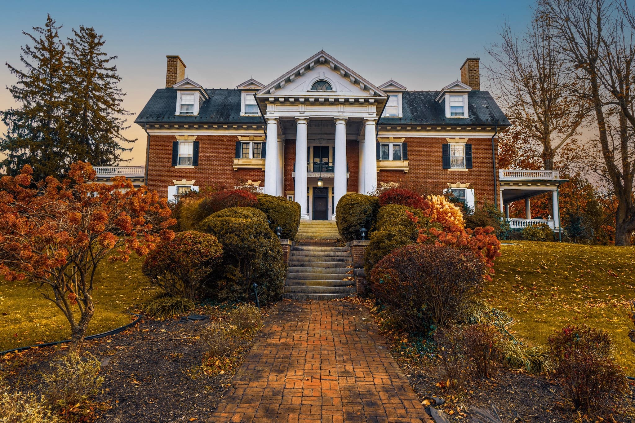 Grand historic brick mansion with prominent white pillars, surrounded by vibrant autumn foliage, conveying a serene and stately atmosphere. Grand historic brick mansion with prominent white pillars, surrounded by vibrant autumn foliage, conveying a serene and stately atmosphere.