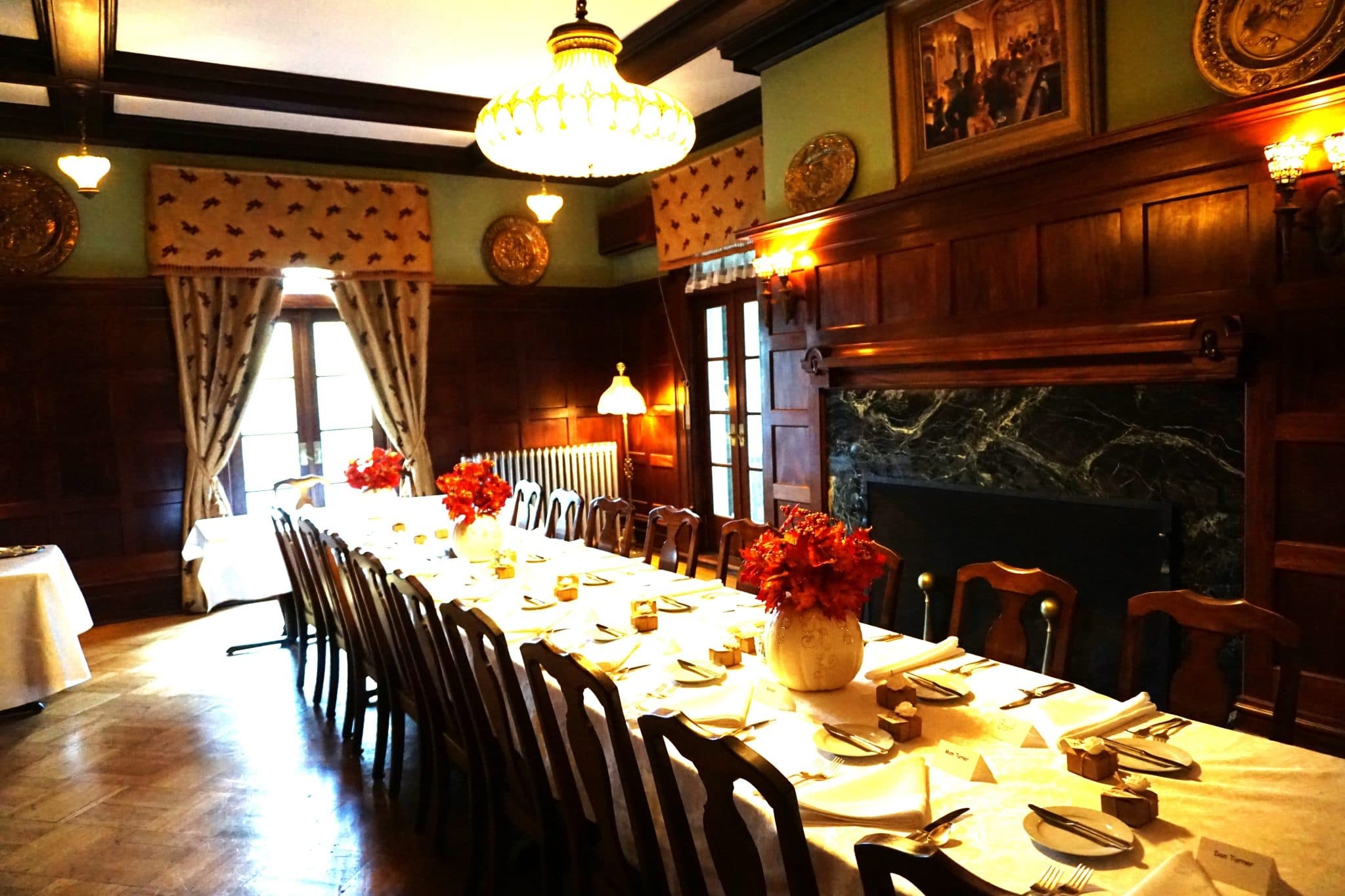 Elegant dining room with a long table set for a formal dinner. Warm lighting, wood paneling, and decorative plates create a vintage, refined ambiance. Elegant dining room with a long table set for a formal dinner. Warm lighting, wood paneling, and decorative plates create a vintage, refined ambiance.