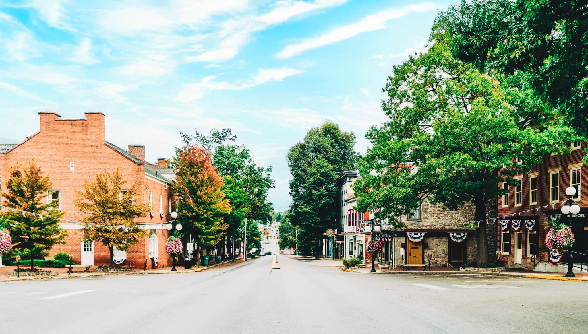 A quiet small-town street with historic brick buildings on both sides, lined with lush trees under a clear blue sky, creating a nostalgic and serene atmosphere. A quiet small-town street with historic brick buildings on both sides, lined with lush trees under a clear blue sky, creating a nostalgic and serene atmosphere.