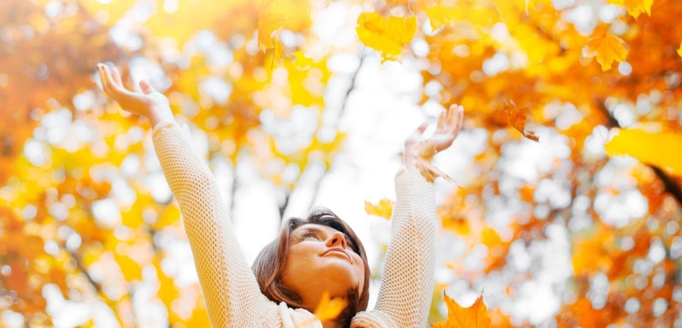 Woman joyfully lifts her arms amidst vibrant autumn leaves, wearing a cozy sweater. The scene conveys happiness and the beauty of fall foliage. Woman joyfully lifts her arms amidst vibrant autumn leaves, wearing a cozy sweater. The scene conveys happiness and the beauty of fall foliage.