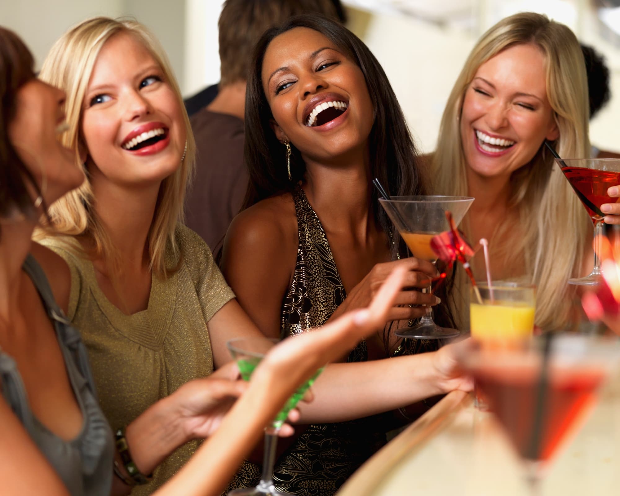 Four women sit at a bar, laughing and holding colorful cocktails. The atmosphere is joyful and lively, conveying a sense of friendship and celebration. Four women sit at a bar, laughing and holding colorful cocktails. The atmosphere is joyful and lively, conveying a sense of friendship and celebration.