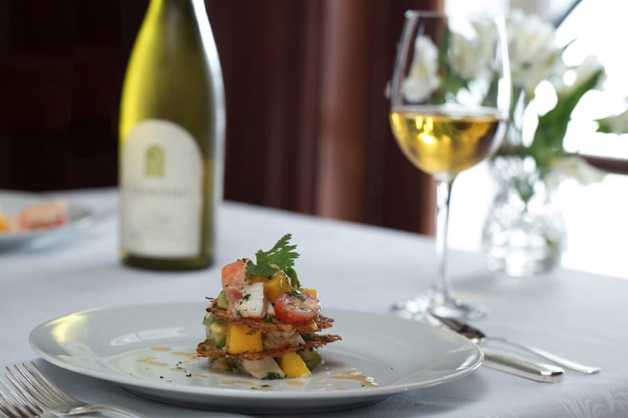 Elegant dining setup with a gourmet vegetable stack on a white plate, paired with a bottle of white wine and a glass. Soft, inviting ambiance.